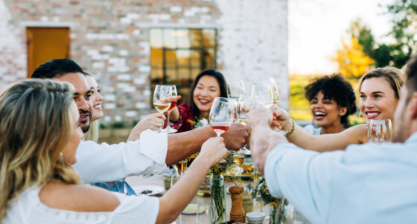 A diverse group of friends laughing and toasting wine glasses at an outdoor supper club dinner