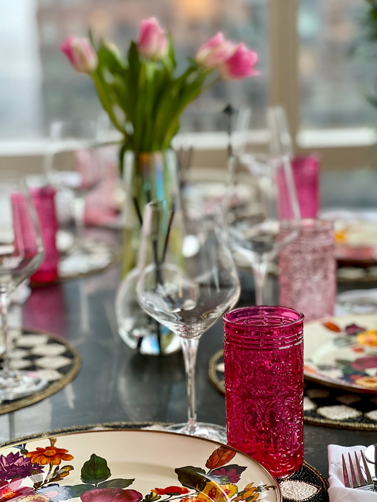 An elegantly set dinner table with floral plates and pink glassware